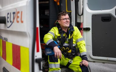 Työntekijä istumassa työauton perällä turvaliivissä ja kypärä kädessä.