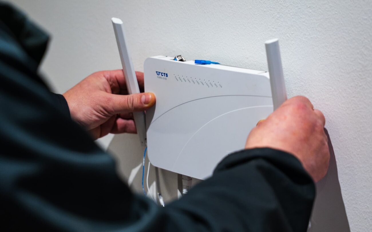 Henkilö asentaa valkoista valokuitu reititintä seinälle.