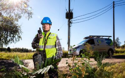 Oulun Seudun Sähkön työntekijä turvaliivissä ja kypärässä tutkimassa maastoa tien varressa.