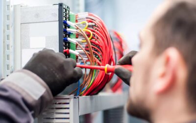 Henkilö työskentelee sähköjohtojen luona ja asentaa niitä paikoilleen. Taustalla näkyy paljon erilaisia ja eri värisiä sähköjohtoja rykelmittäin.