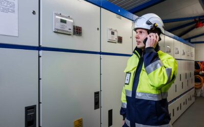 Oulun Seudun Sähkön työntekijä turvaliivissä ja kypärässä seisoo sähkölaitoksen tiloissa.