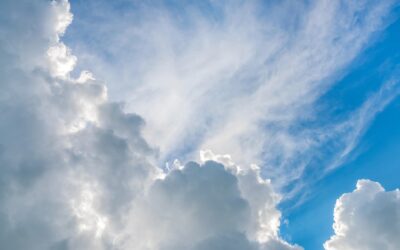 Kuva pilvien peittämästä sinisestä taivaasta. Pilvien takaa paistaa hieman aurinko.