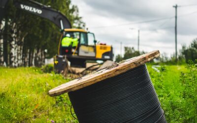 Etualalla on suuri kaapelikella ja taustalla keltainen kaivinkone.
