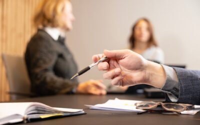 Työntekijä käsittelee asiakirjoja kokoushuoneessa, kuvan taustalla kollegoita epätarkkana.