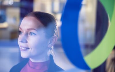 Oulun Seudun Sähkön työntekijä seisomassa osuuskunnan logolla varustetun lasiseinän edessä.