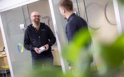 Kaksi Oulun Seudun Sähkön työntekijää keskustelee toimistokoppien edessä hymyillen.