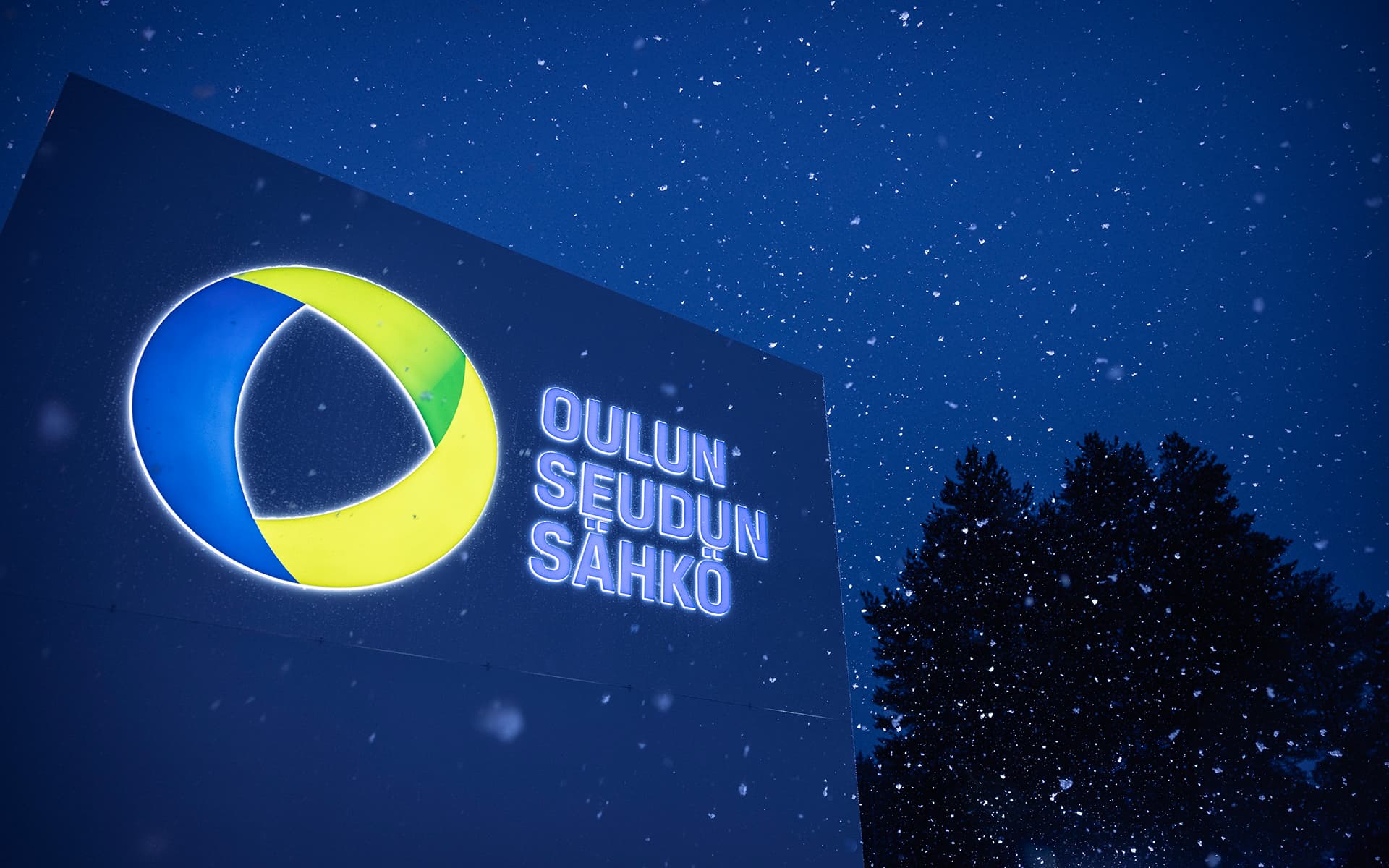 Oulun Seudun Sähkön kyltti iltahämärässä kevyessä lumisateessa.